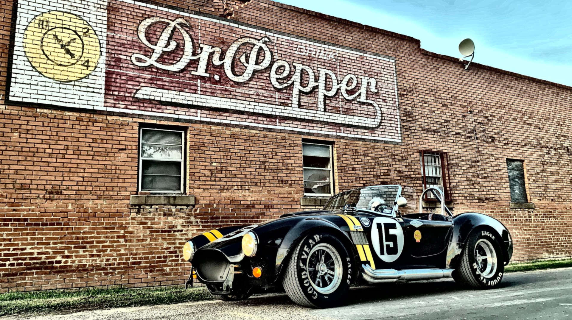 Vintage Cobra car with number 15 in front of a brick building with Dr Pepper signage.